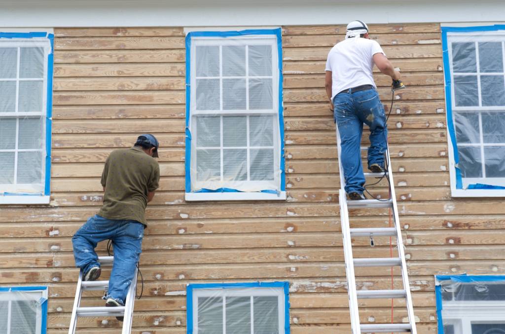 Painting crew working on house siding with ladders