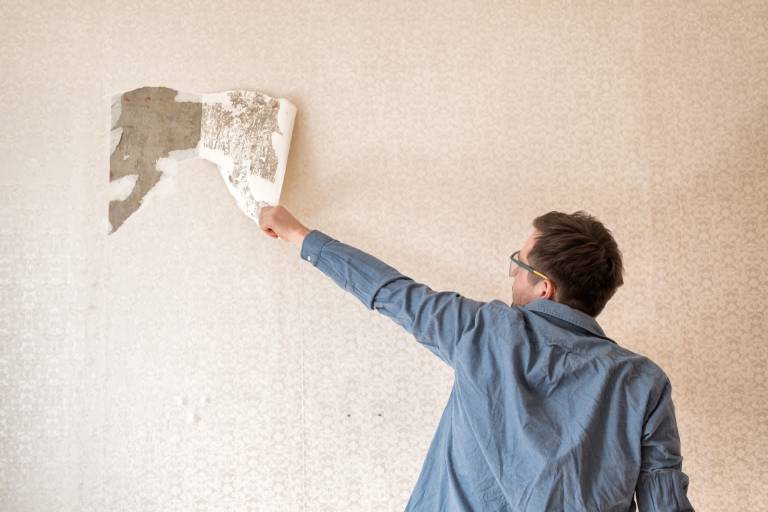 Painter removing old wallpaper from a wall